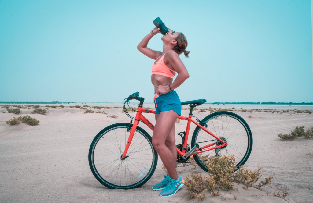 fit woman drinking water while resting on a bike